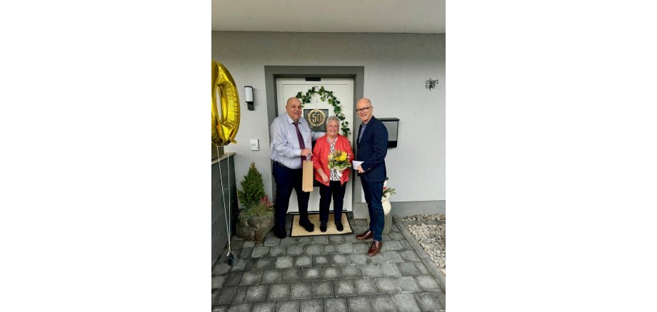 Eheleute Faber erhalten ein Präsent zur goldenen Hochzeit von Oberbürgermeister Dirk Meid 2 Männer und eine Frau stehe vor einer Haustür und haben Präsente in den Händen