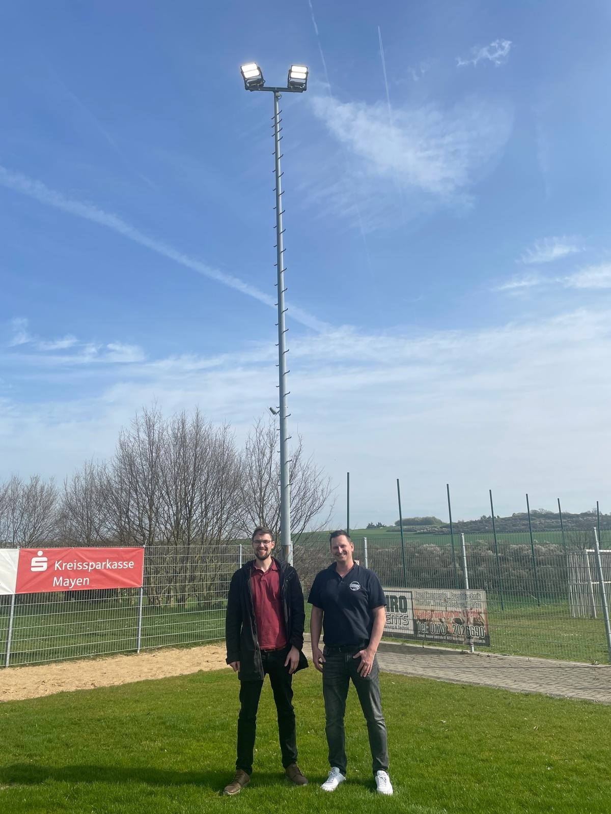 2 Männer stehen vor einem Flutlichtmast