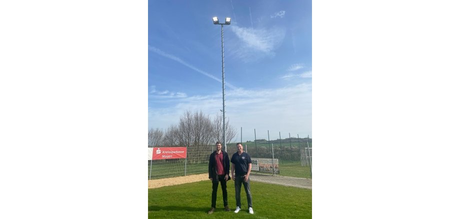 Klimaschutzmanager Helge Lippert (links) und Hendrik Machoi von „Kandem Leuchten GmbH“ freuen sich über die neue LED-Beleuchtung 2 Männer stehen vor einem Flutlichtmast