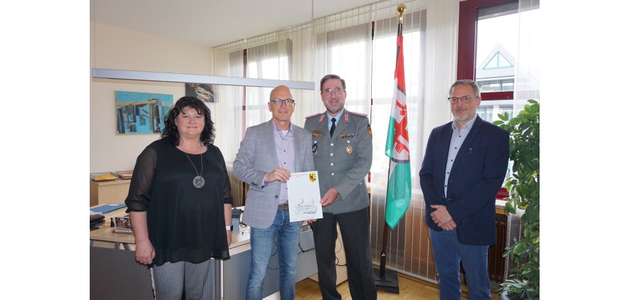 Eine Frau und drei Herren stehen für ein Bild zusammen - 2 davon halten einen Vertrag in den Händen