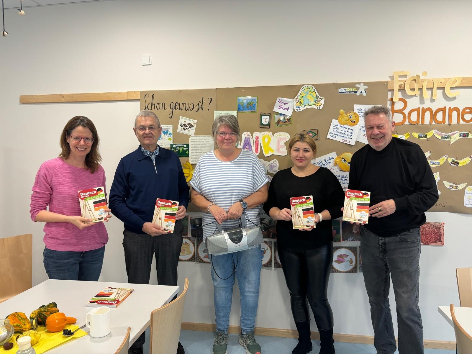 5 Personen sind zu sehen. 4 Personen halten jeweils ein Exemplar des Sprachförderungsbuch hoch, die Person in der Mitte hält einen CD-Spieler in den Händen