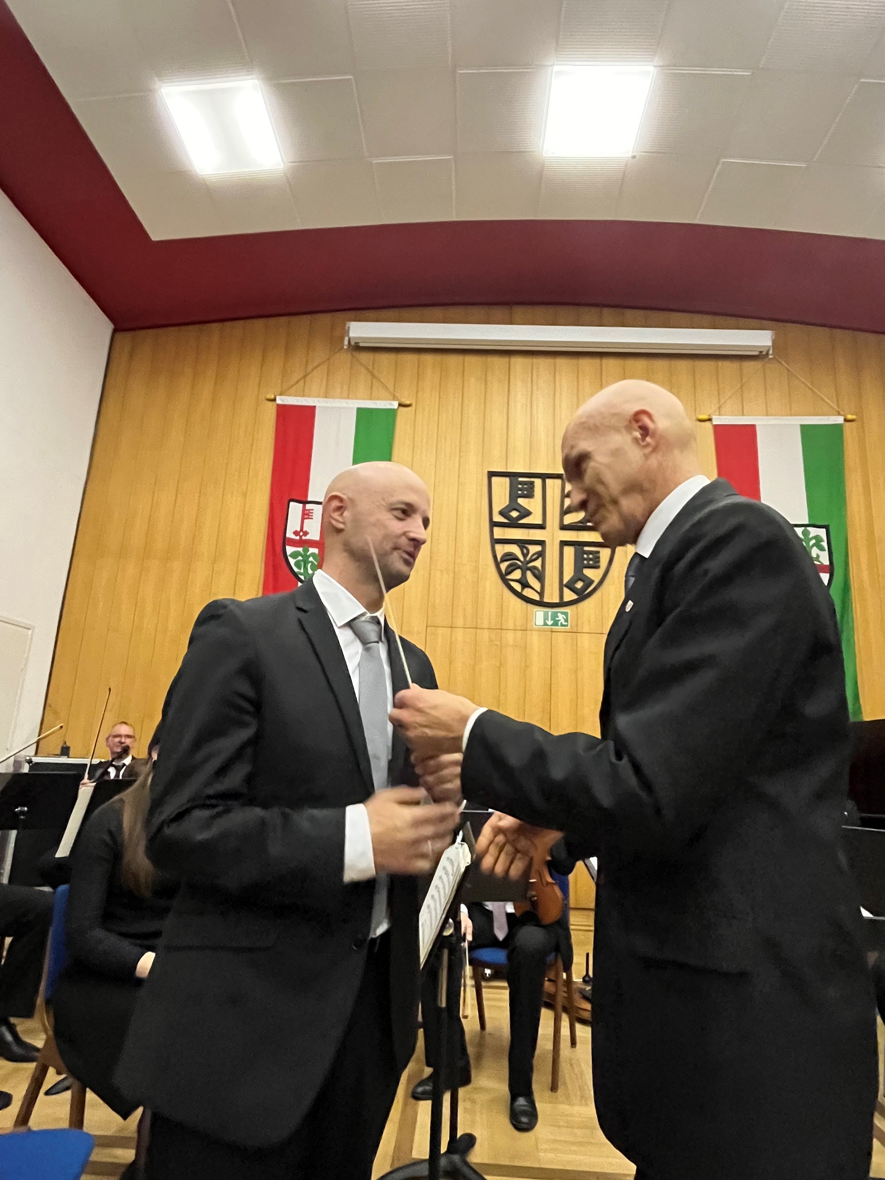 Ein Mann übergibt einem anderen einen Taktstock