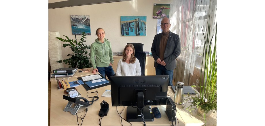 Ein Mädchen sitzt am Schreibtisch, daneben eine Frau und ein Mann