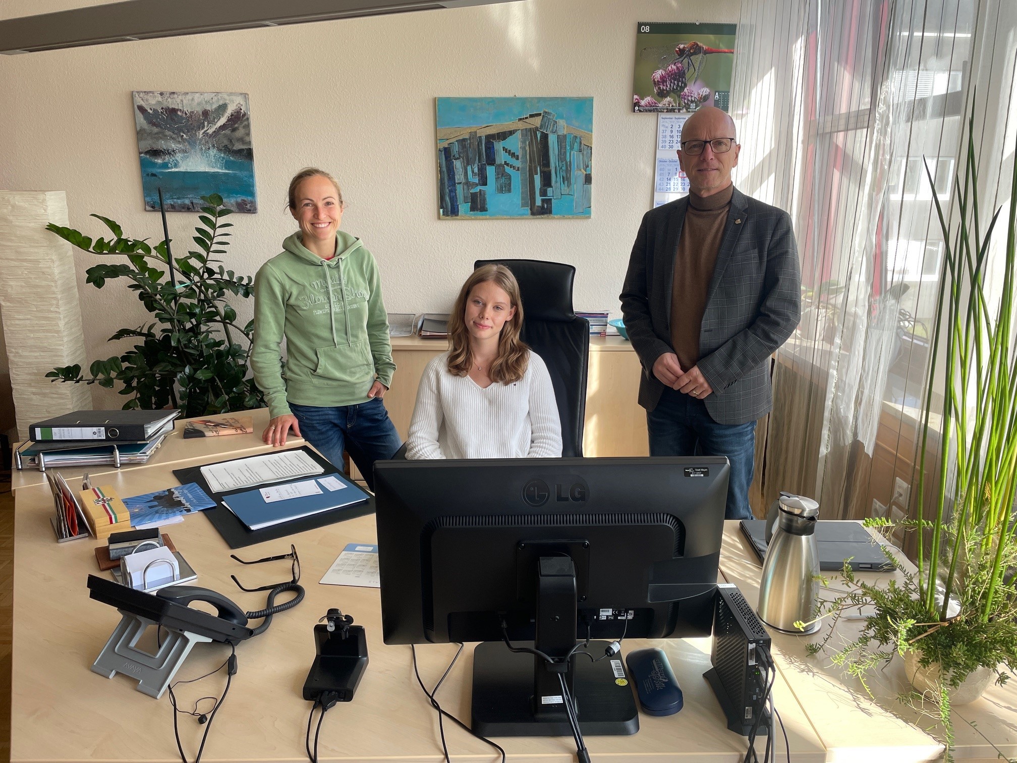 Ein Mädchen sitzt am Schreibtisch, daneben eine Frau und ein Mann