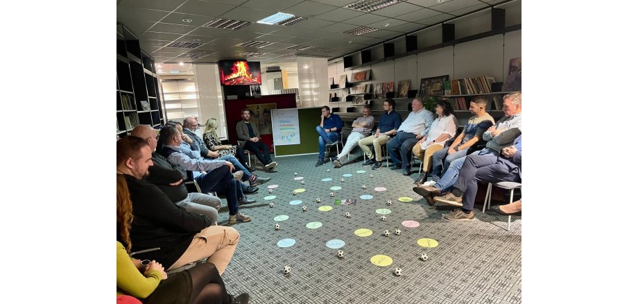 Ein reger Austausch in entspannter Atmosphäre beim ersten Kaminabend Mehrere Personen sitzen in einem Stuhlkreis zusammen - in der Mitte liegen verschiedene Gegenstände