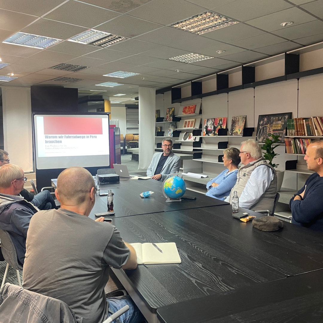 Mehrere Personen sitzen an einem Tisch und tauschen sich aus - im Hintergrund ist eine Leinwand zu sehen