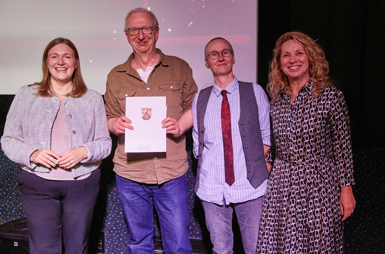 4 Personen stehen für ein Foto zusammen, einer hält eine Urkunde in den Händen