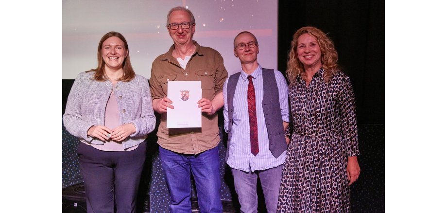 4 Personen stehen für ein Foto zusammen, einer hält eine Urkunde in den Händen