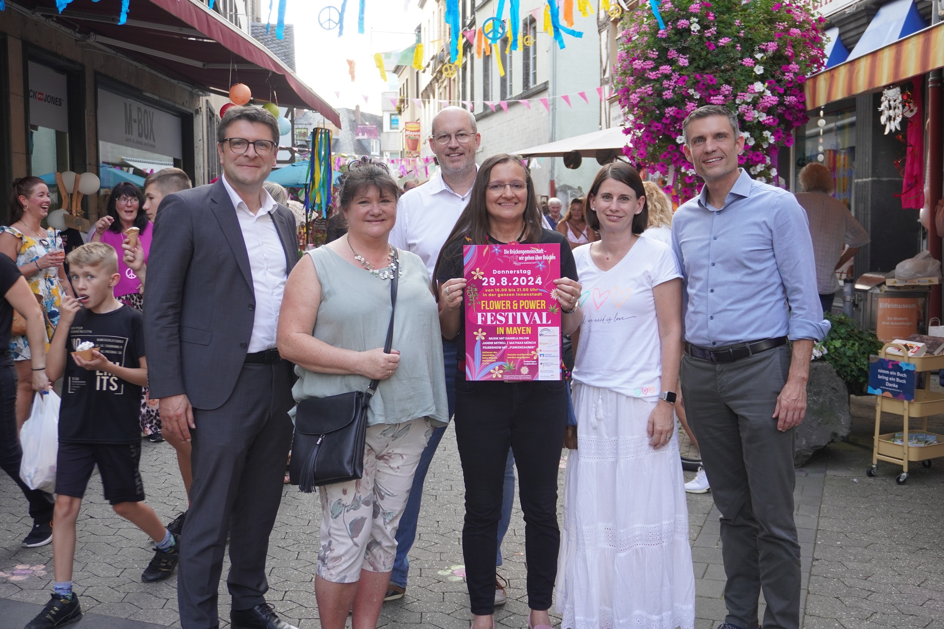 6 Personen stehen in einer Einkaufsstraße - eine hält das Plakat zur Veranstaltung in den Händen
