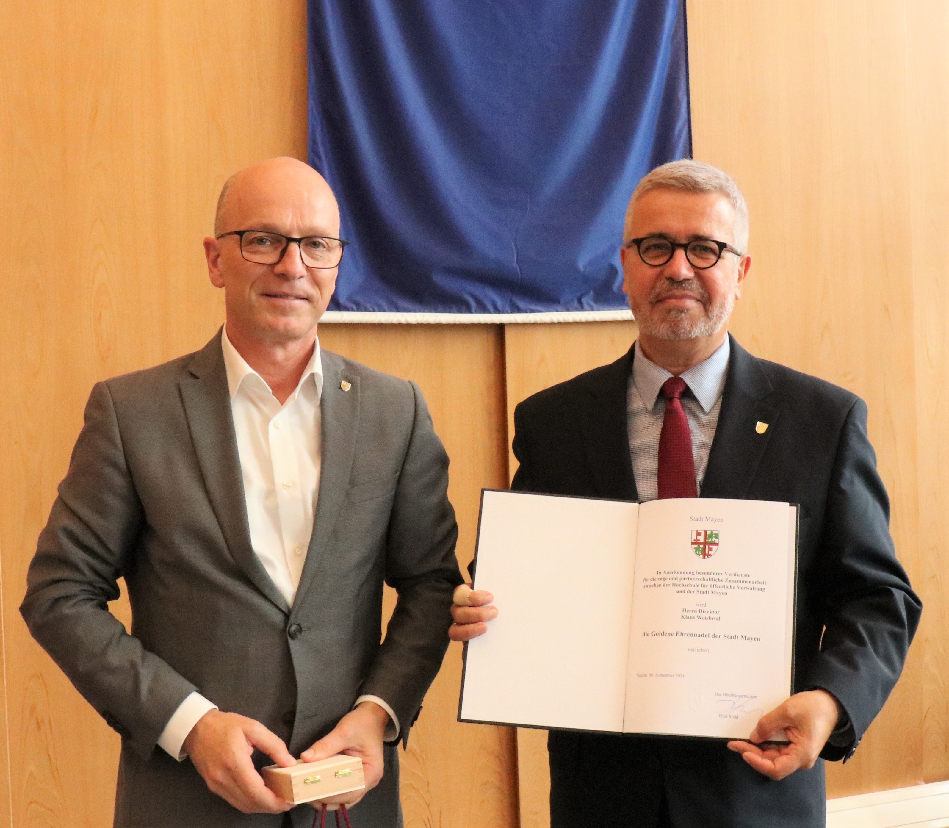 2 Männer in Anzug - einer hält eine Urkunde in der Hand