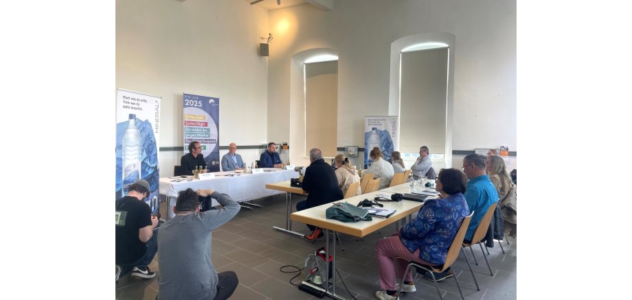 3 Personen sitzen einer Gruppe von Menschen entgegen und sprechen