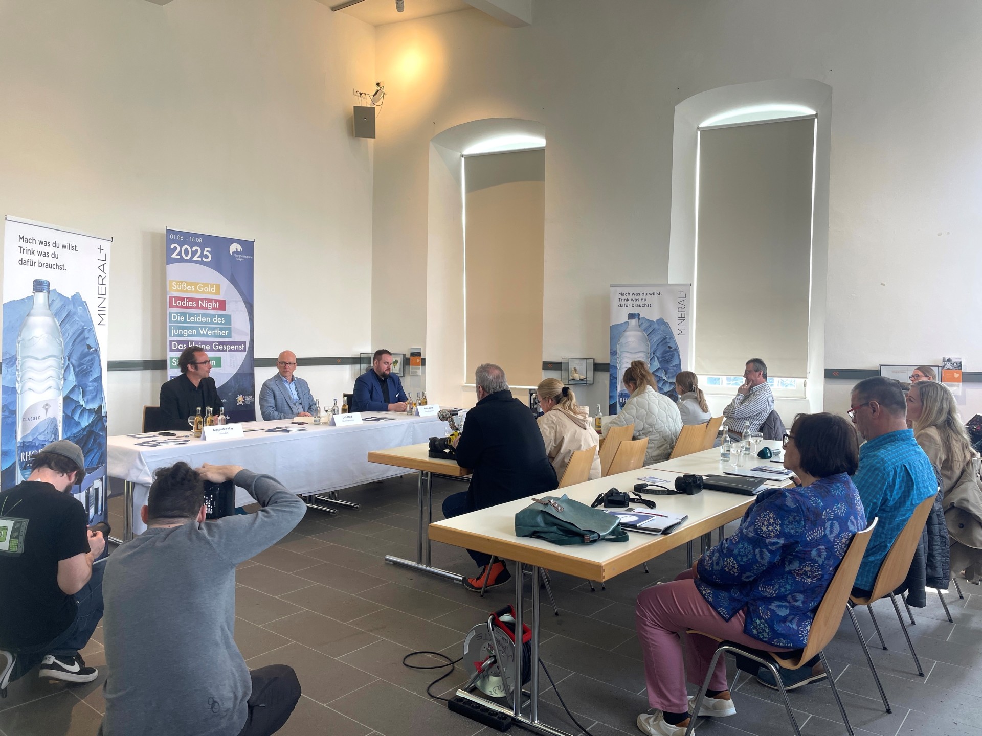 3 Personen sitzen einer Gruppe von Menschen entgegen und sprechen