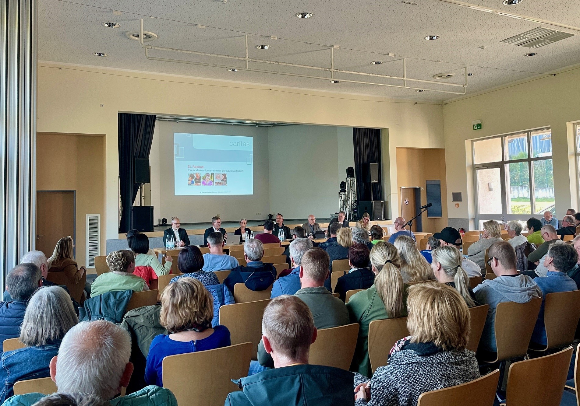 Eine vollbesetzte Halle - Menschen schauen sich eine Präsentation an