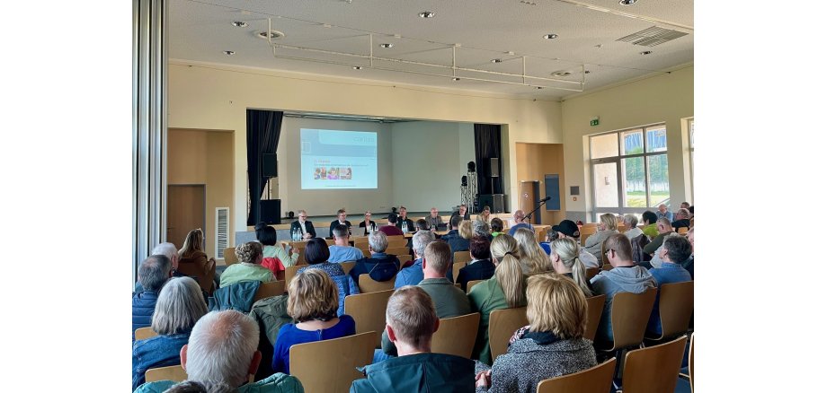 Eine vollbesetzte Halle - Menschen schauen sich eine Präsentation an