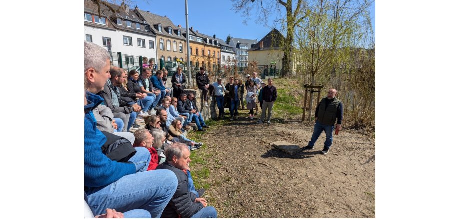 Eine Gruppe von Menschen sitzt in einem Halbkreis vor einem Mann, der etwas erklärt