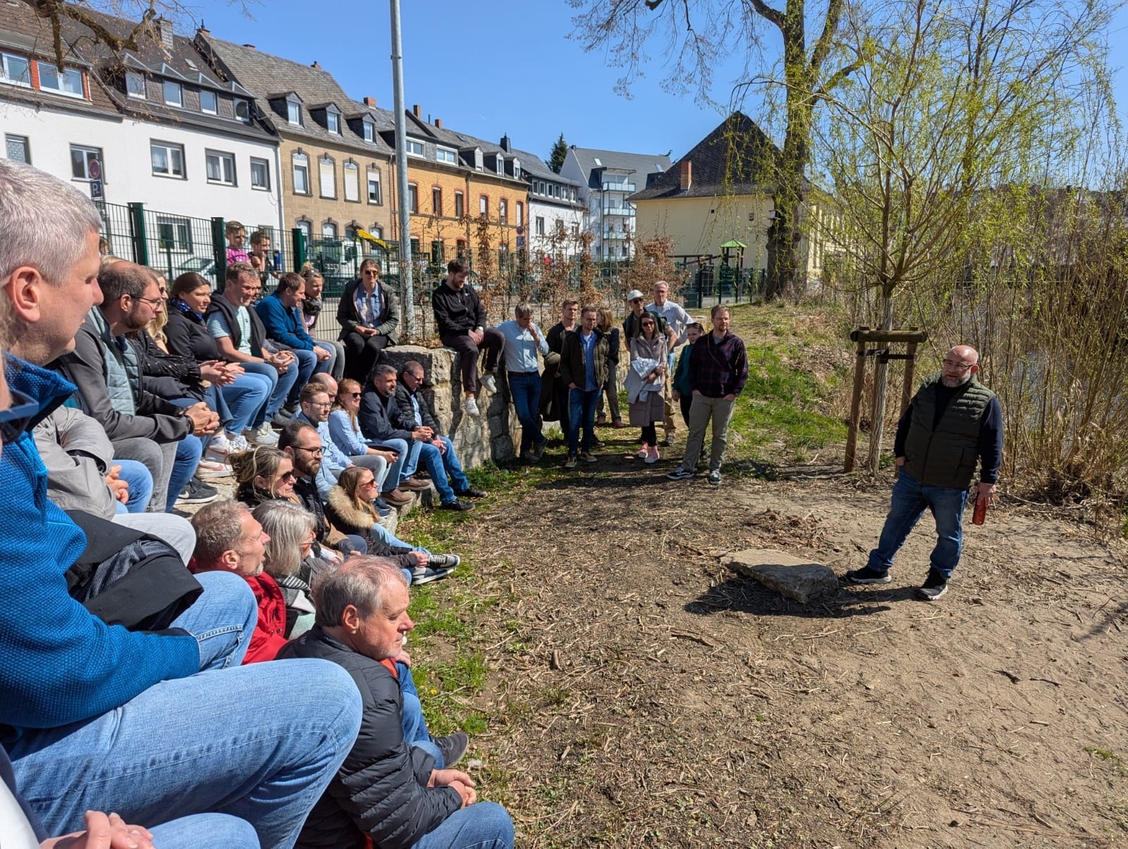 Eine Gruppe von Menschen sitzt in einem Halbkreis vor einem Mann, der etwas erklärt