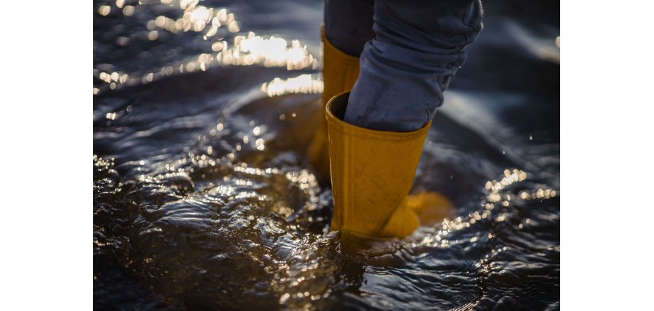 Beine einer Person, die im Wasser steht und Gummistiefel anhat 
