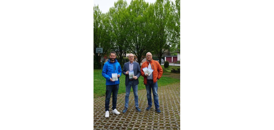 3 Personen stehen zusammen und halten eine Broschüre in den Händen