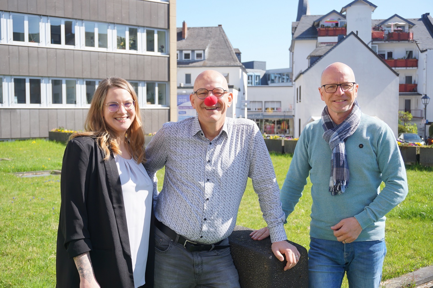 3 Personen stehen für ein Foto zusammen - der Mann in der Mitte hat eine rote Nase