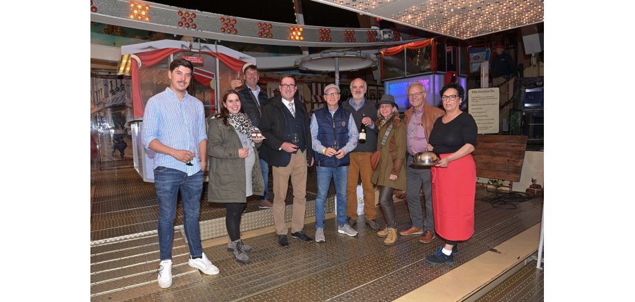 Eine Personengruppe steht im Eingangsbereich vom Riesenrad vor den Gondeln
