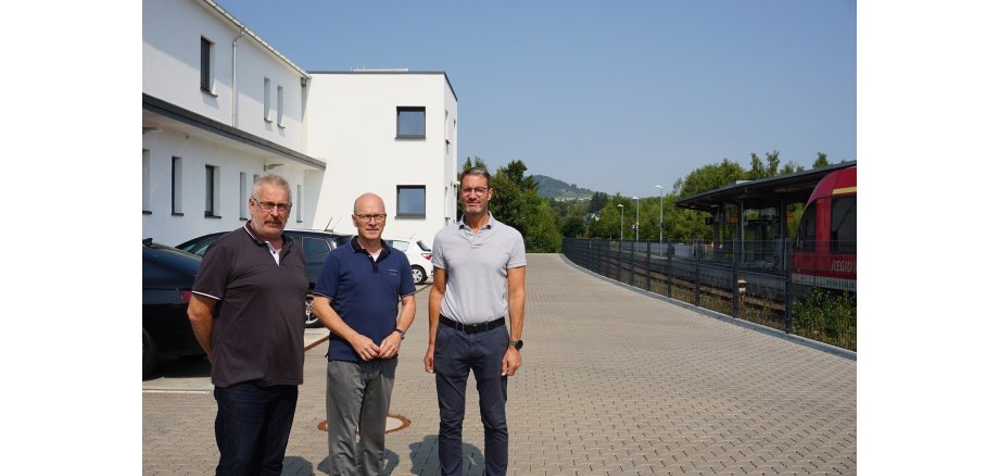 3 Männer stehend auf einem Parkplatz vor einem Gebäude