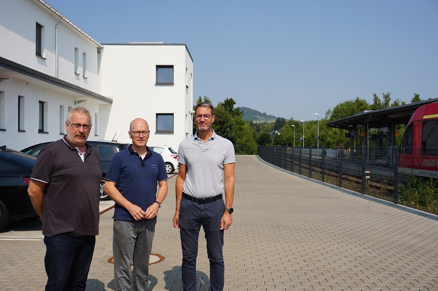 3 Männer stehend auf einem Parkplatz vor einem Gebäude