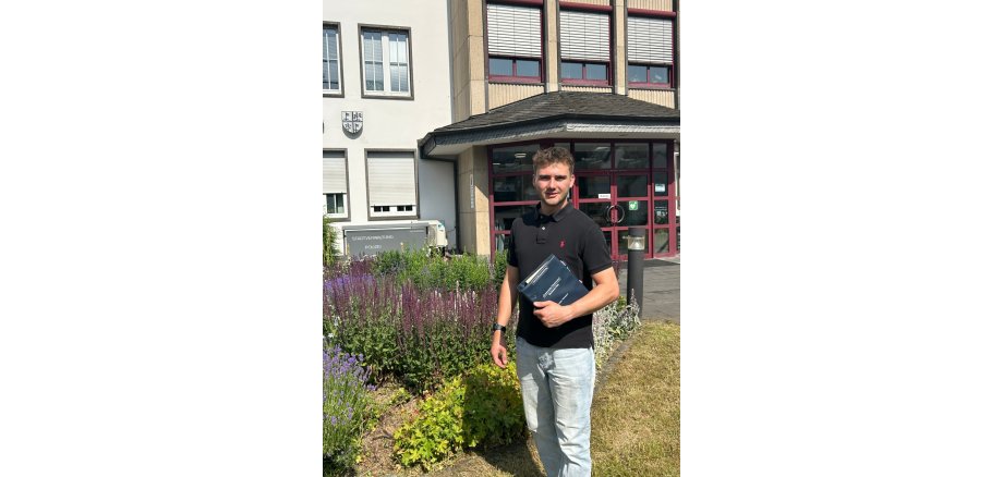 Marius Luxem hält ein Gesetzbuch in der Hand und steht vor der Stadtverwaltung