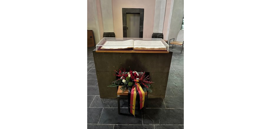 Gedenkfeier am 2. Januar an der Heilig-Geist-Kapelle Mayen Aufgeschlagenes Buch auf einem Sockel. Davor steht ein Blumengesteck