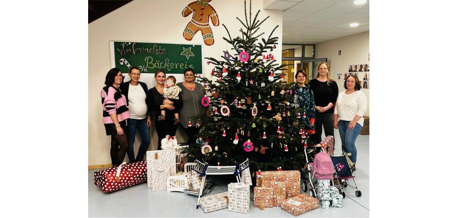 Insgesamt sieben Frauen und ein Baby stehen links und rechts neben einem üppig geschmückten Weihnachtsbaum