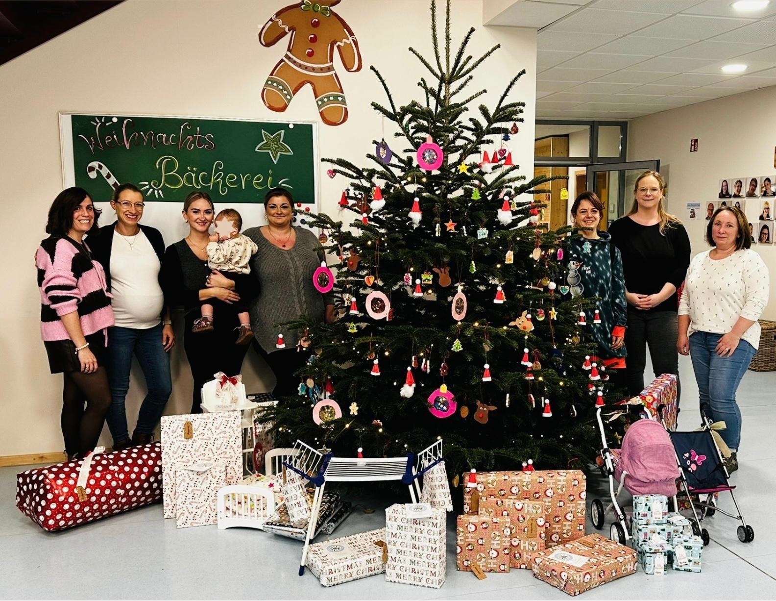 Insgesamt sieben Frauen und ein Baby stehen links und rechts neben einem üppig geschmückten Weihnachtsbaum