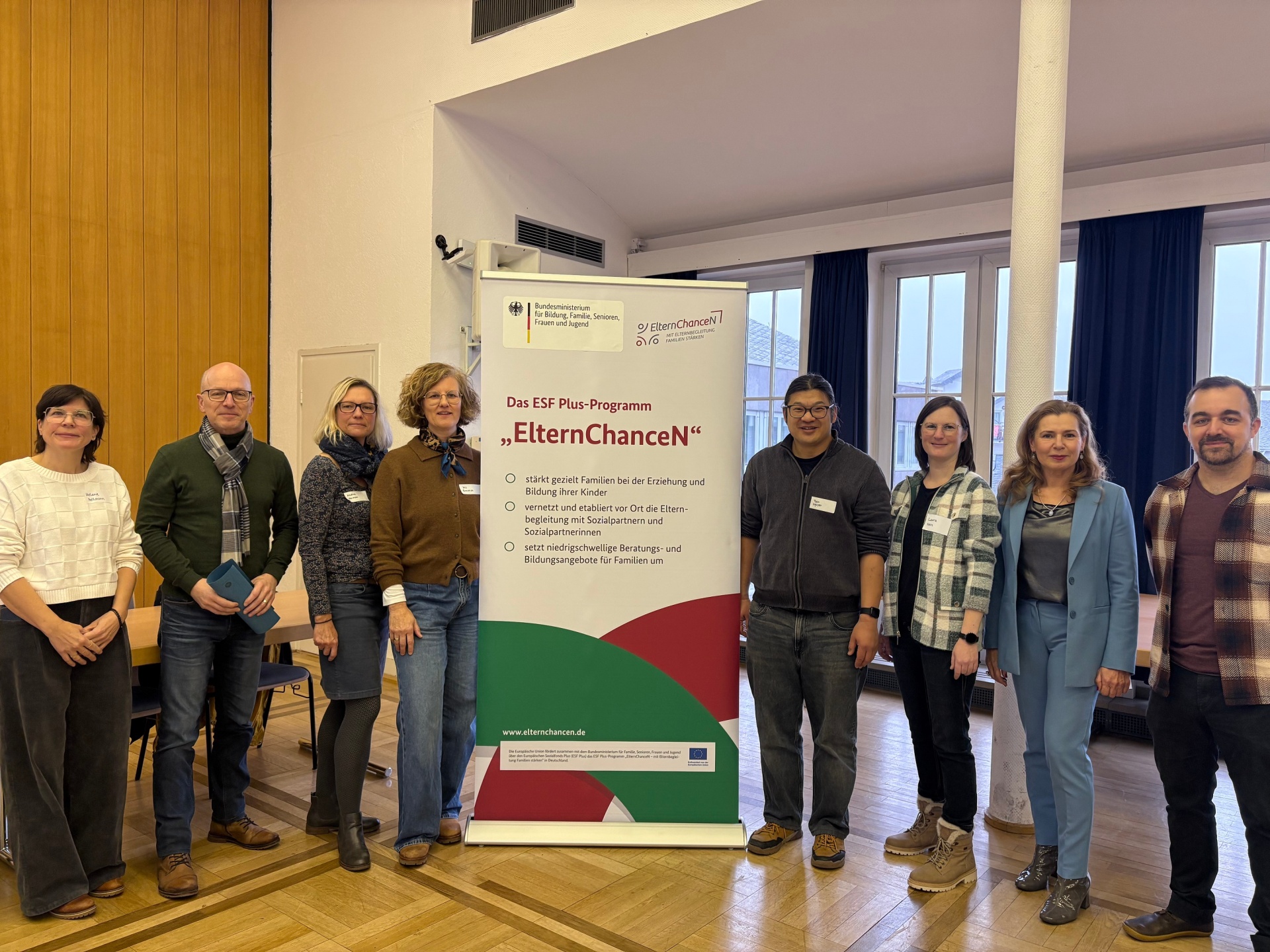 Zahlreiche Vertreterinnen und Vertreter aus unterschiedlichsten Bereichen stehen rechts und links neben einem Roll-Up im Sitzungssaal