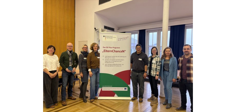 Zahlreiche Vertreterinnen und Vertreter aus unterschiedlichsten Bereichen stehen rechts und links neben einem Roll-Up im Sitzungssaal