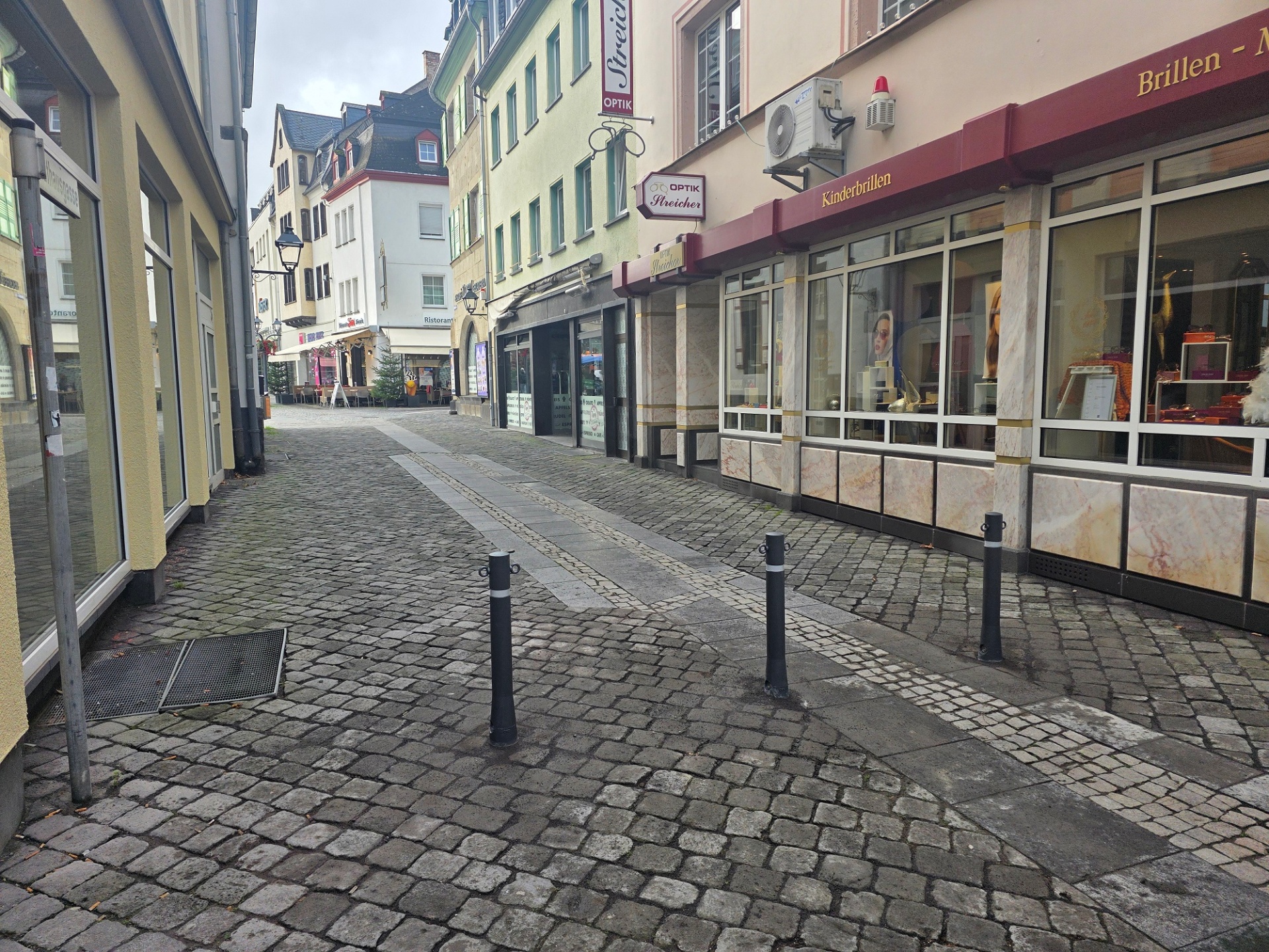 Drei graue Poller stehen in einer Fußgängerzone