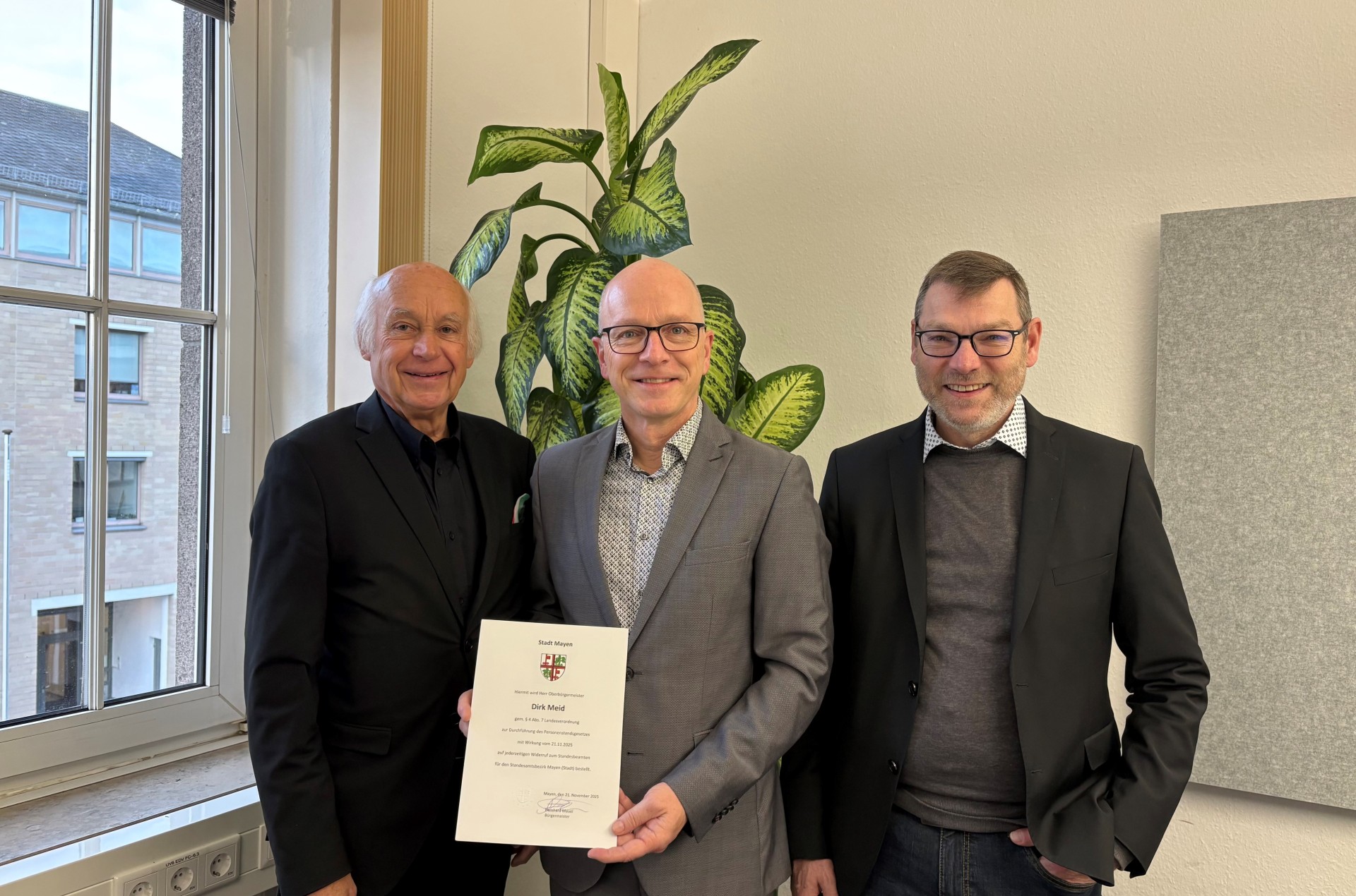 Bürgermeister Bernhard Mauel, Oberbürgermeister Dirk Meid und Beigeordneter Thomas Schroeder stehen neben einem Fenster vor einer Pflanze. OB Meid hält seine Urkunde in der Hand