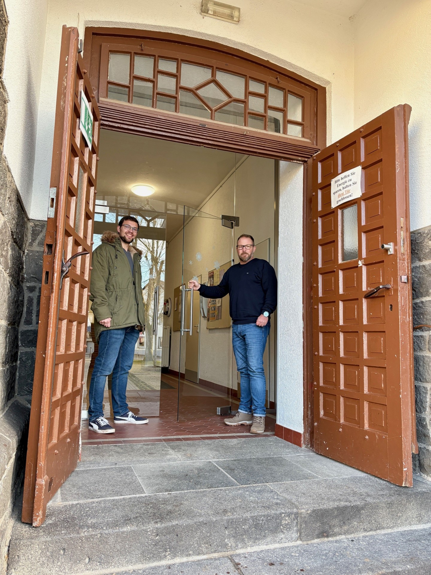 Klimaschutzmanager Helge Lippert (links) und Ortsvorsteher Sascha Flinsch stehen vor dem neuen Doppelflügel-Glaswindfang
