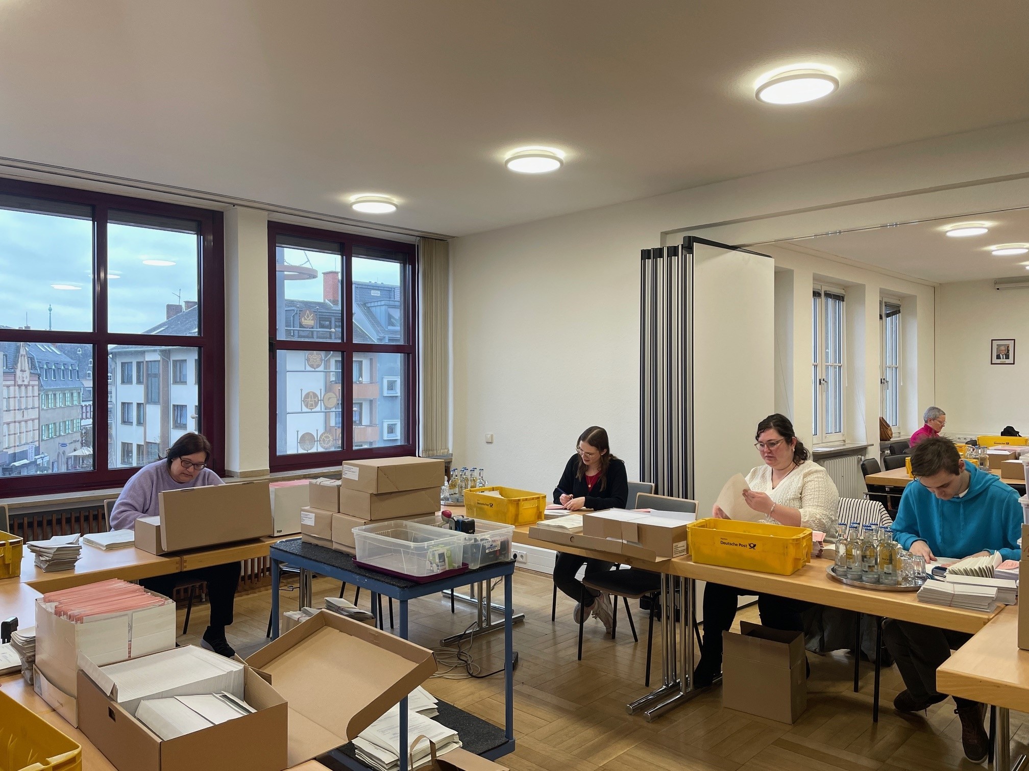 Mehrere Personen sitzen an Tischen und bereiten die Briefwahlunterlagen vor
