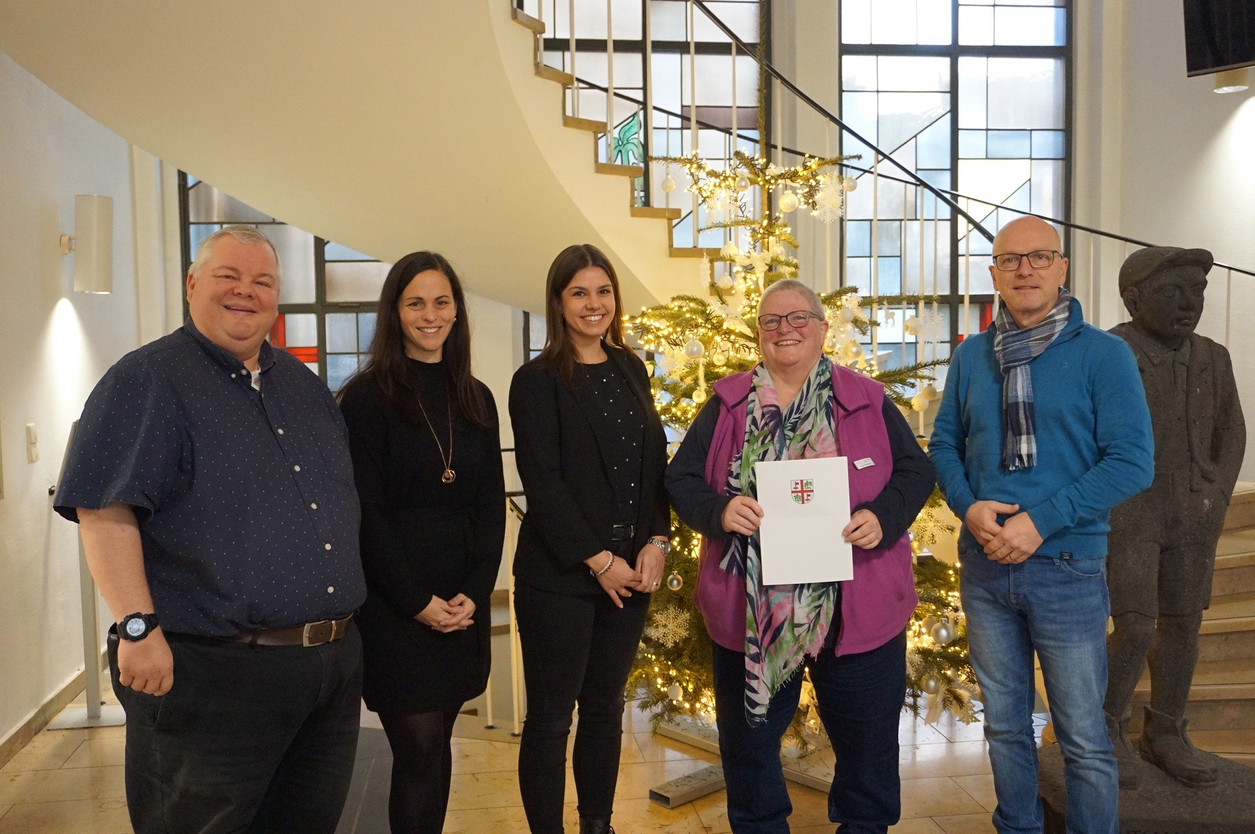 5 Personen stehen vor einer Treppe - eine Person hält eine Urkunde in der Hand