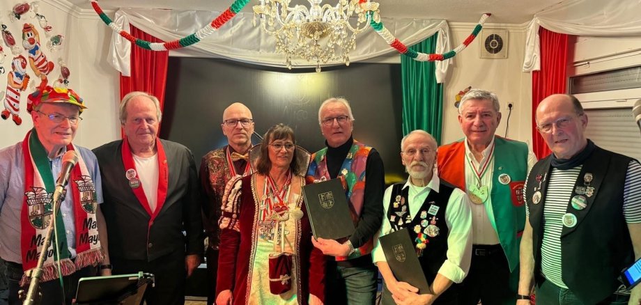 Die Mitglieder der Band freuen sich über die Anerkennung der Stadt Mayen 8 Personen in Kostümen stehen für ein Foto in einem geschmückten Raum zusammen