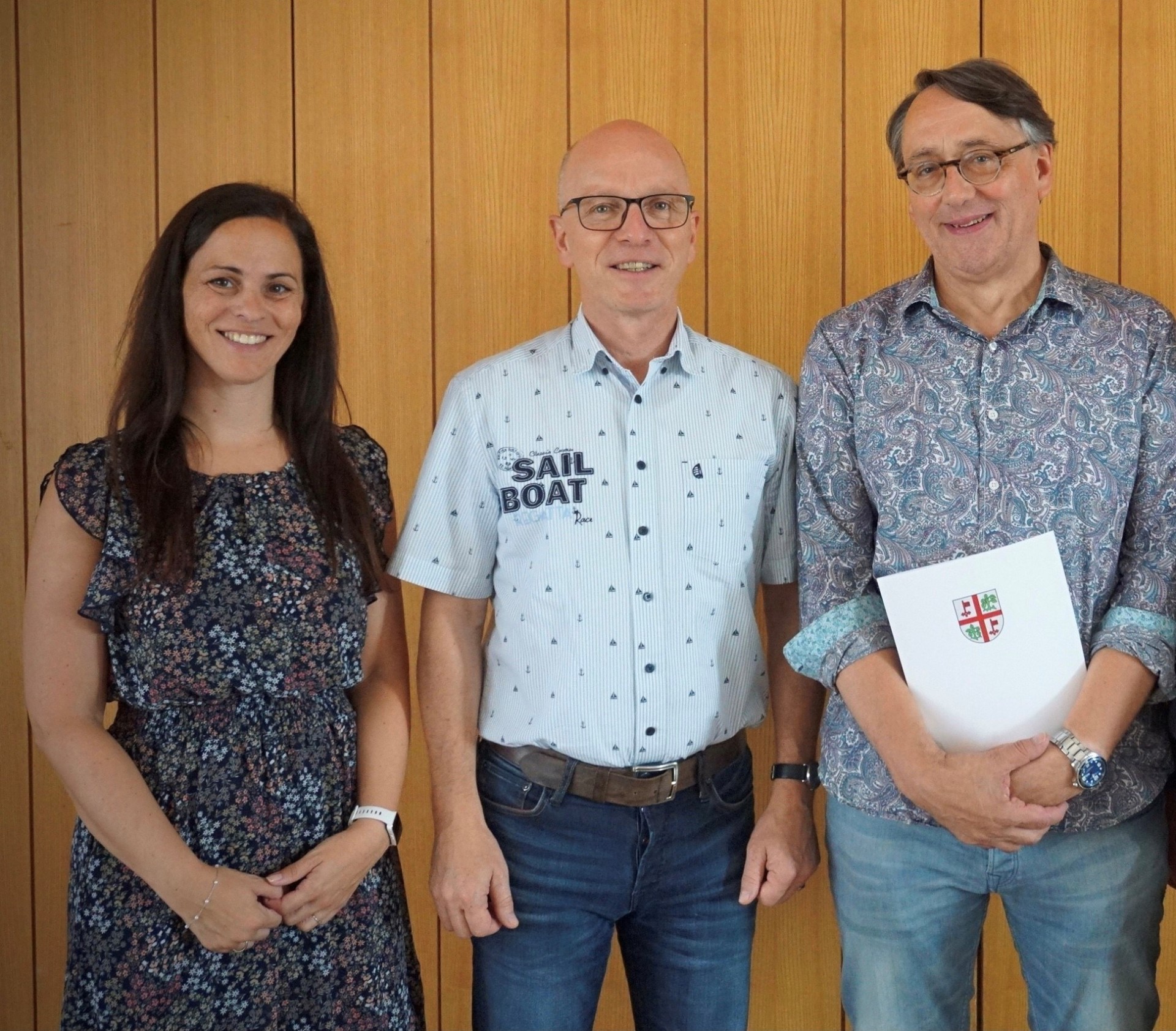 3 Personen stehen zusammen, einer davon hält eine Urkunde in den Händen