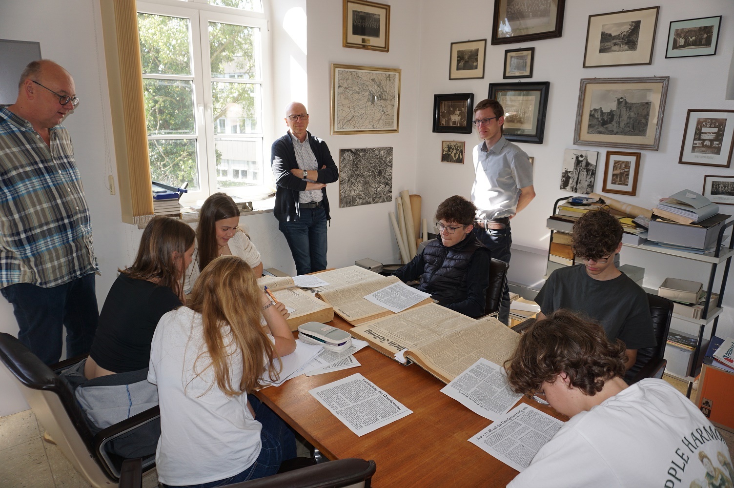 Mehrere Personen sitzen und stehen an einem Tisch und recherchieren