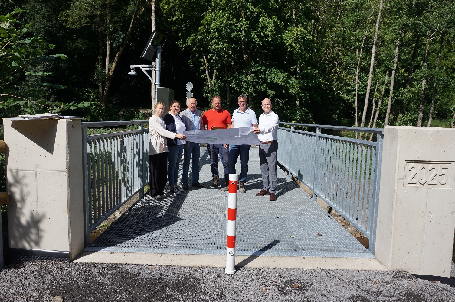Mehrere Personen stehen auf einer Brücke und halten einen Plan in der Hand