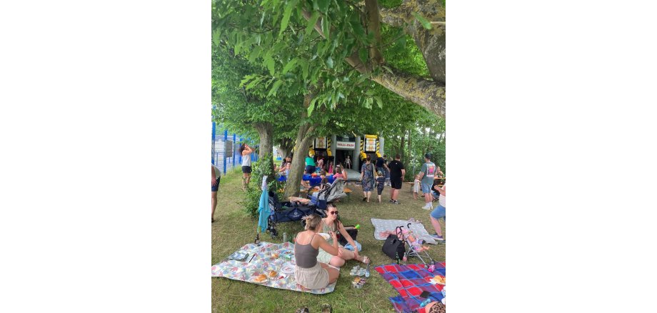 Eltern und Kinder auf einer Wiese. Im Hintergrund steht eine Hüpfburg.