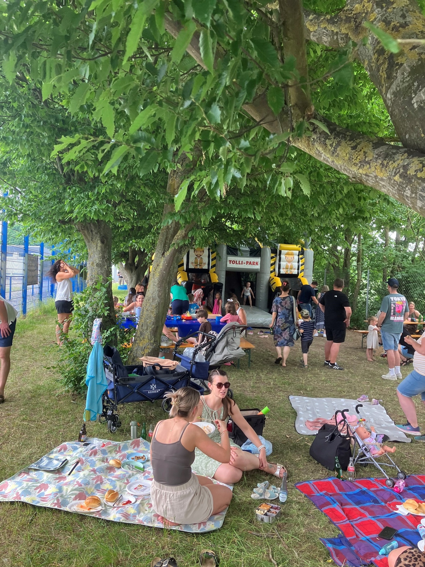 Eltern und Kinder auf einer Wiese. Im Hintergrund steht eine Hüpfburg.