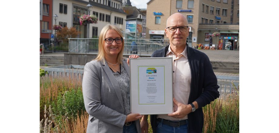 Oberbürgermeister Dirk Meid und Fairtrade-Beauftragte Janine Pitzen halten gemeinsam die Fairtrade-Urkunde in den Händen.
