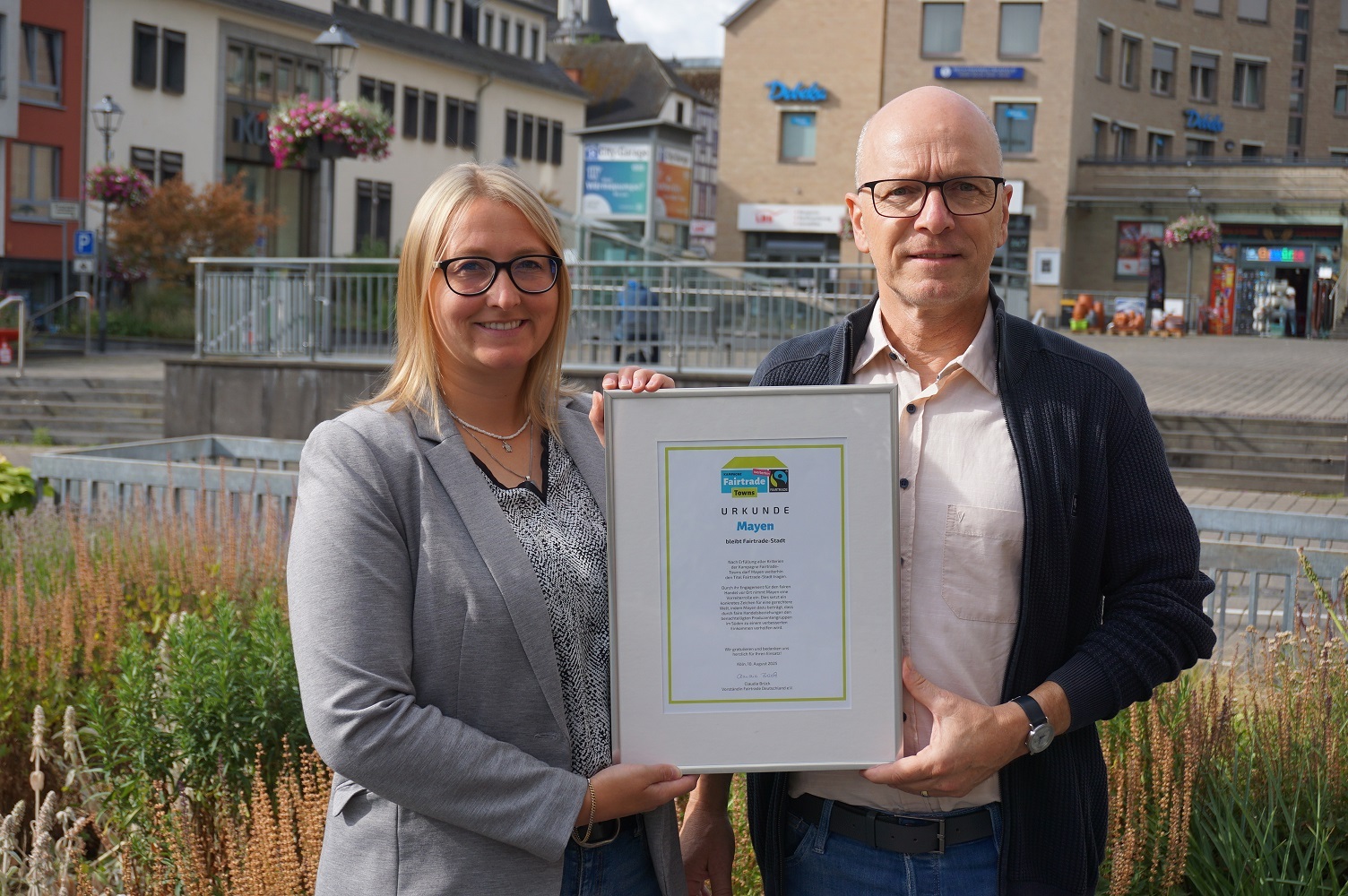 Oberbürgermeister Dirk Meid und Fairtrade-Beauftragte Janine Pitzen halten gemeinsam die Fairtrade-Urkunde in den Händen.