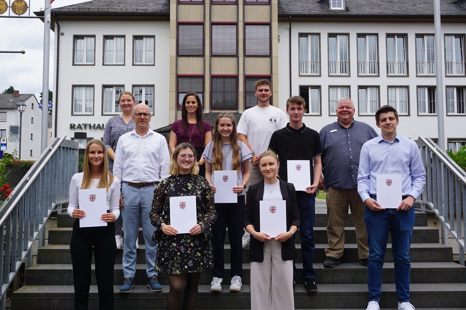 v.l.n.r.: Nele Marie Schulz, Gleichstellungsbeauftragte Janine Pitzen, Oberbürgermeister Dirk Meid, Pauline Montada, Büroleiterin Jasmin Alter, Nina Lauter, Marius Luxem von der JAV, Emilie Hill, Ben Randy Franzen, Personalratsvorsitzender Wolfgang Goeken und Mario Vallendar Mehrere Personen stehen für ein Gruppenfoto auf einer Treppe vor dem Verwaltungsgebäude