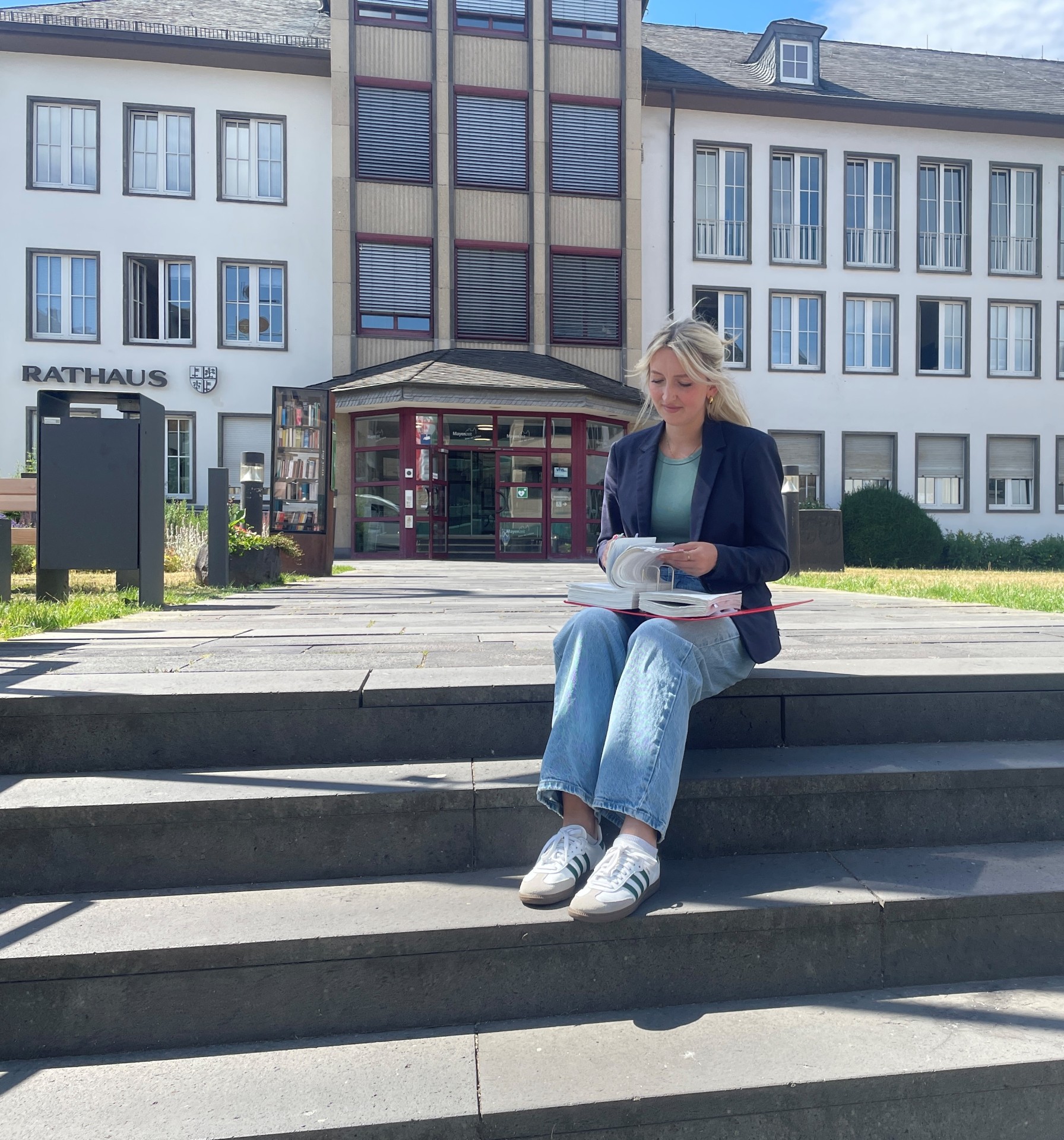 Maria Schultheis befindet sich aktuell in der Ausbildung zur Stadtsekretärin Eine Frau sitzt auf einer Treppe und blättert in einem Gesetzbuch