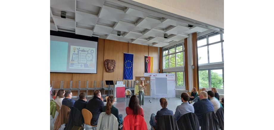 Mehrere Menschen sitzen in einem Halbkreis zusammen und hören einer Frau zu