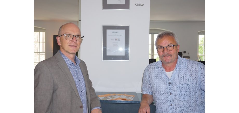 Zwei Männer stehen vor einer eingerahmten Urkunde