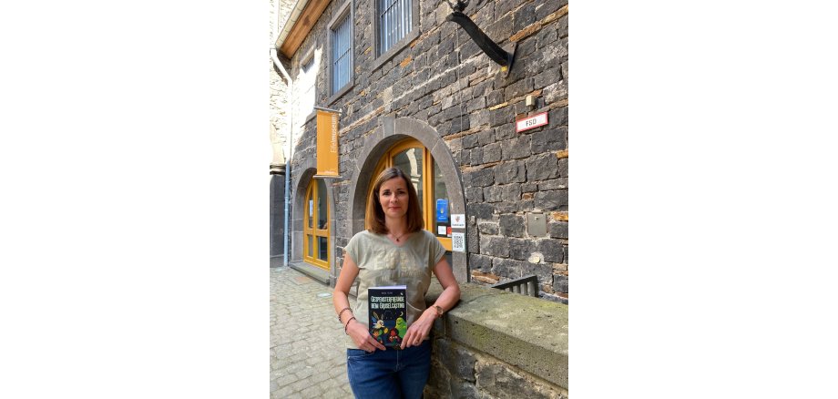 Kinderbuchautorin Verena Freund-Donnhauser steht mit ihrem Buch vor dem Eingang des Eifelmuseums